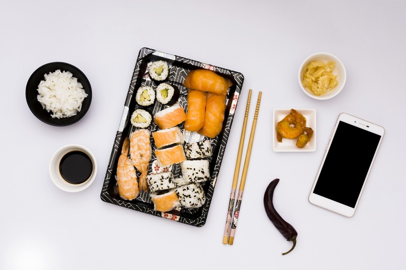 Mesa branca com embalagem de sushi delivery e vários outros acompanhamentos
