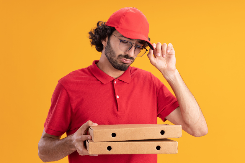 Entregador de pizza olhando para a caixa com fundo amarelo