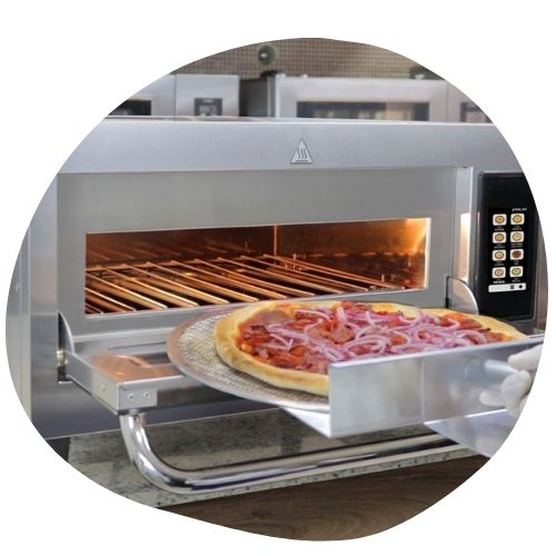 Pizza sendo assada em forno de pizza portátil vermelho ao ar livre com uma fatia já pronta sendo retirada.