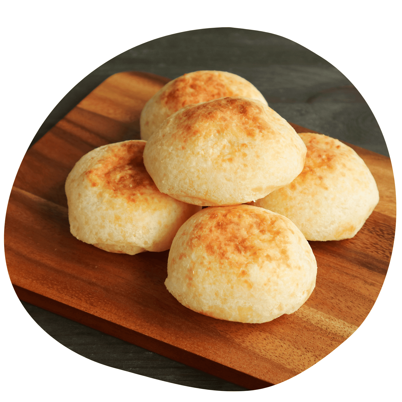 Imagem circular de cinco pães de queijo dourados empilhados sobre uma tábua de madeira. Fundo escuro realçando a textura crocante e o tom amarelado dos salgados.