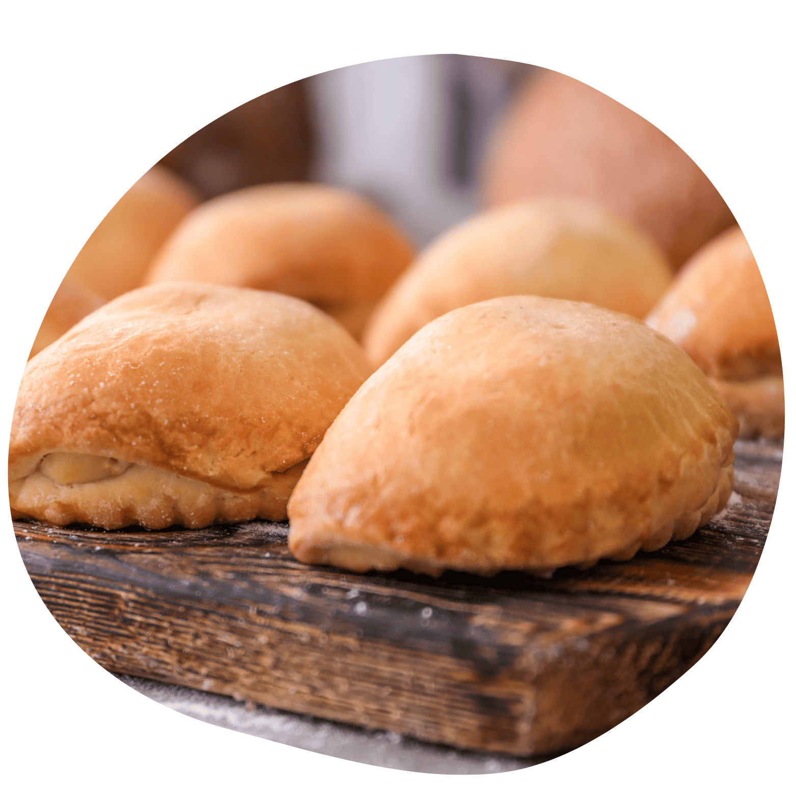 Close-up de salgados assados tipo calzone ou pastel de forno sobre uma tábua de madeira escura com polvilho de farinha.