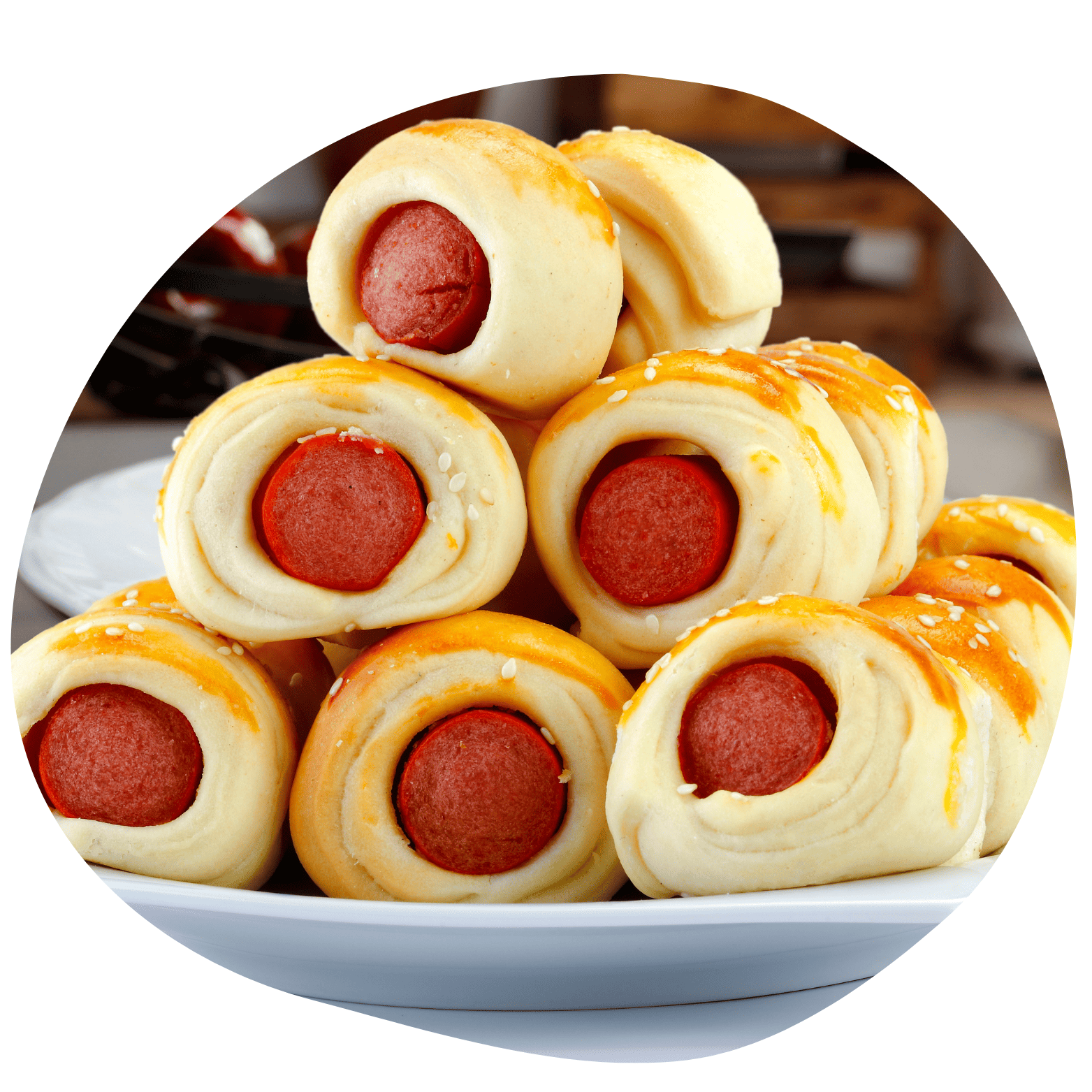 Pilha de enroladinhos de salsicha assados e dourados com sementes de gergelim. Dispostos em um prato branco com fundo desfocado.