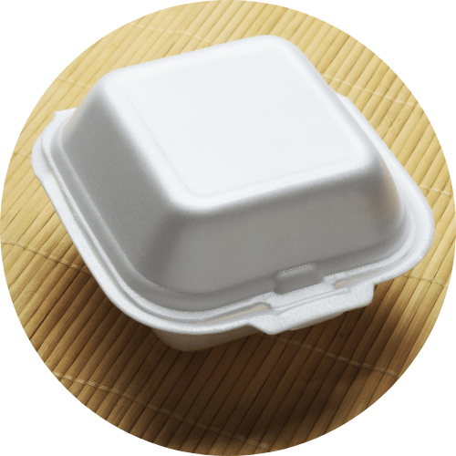 Embalagem quadrada de isopor branco. Abaixo do objeto há um jogo americano de bambu envelhecido, da cor bege.