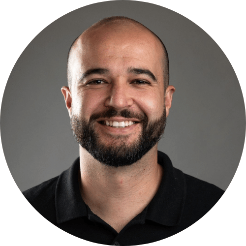 Rapha Silva é um homem sorridente de barba preta aparada e cabeça raspada, vestindo camisa polo preta, fotografado sobre fundo cinza neutro em retrato profissional circular
