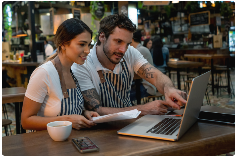 foto mostra um homem e uma mulher em um restaurante em frente a um notebook